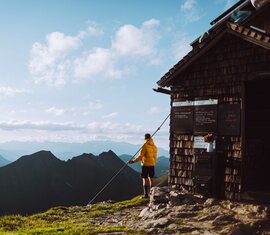 Wanderer vor einer Berghütte mit atemberaubendem Panorama der umliegenden Gipfel und Täler. | © SalzburgerLand Tourismus - Denis Cebulec