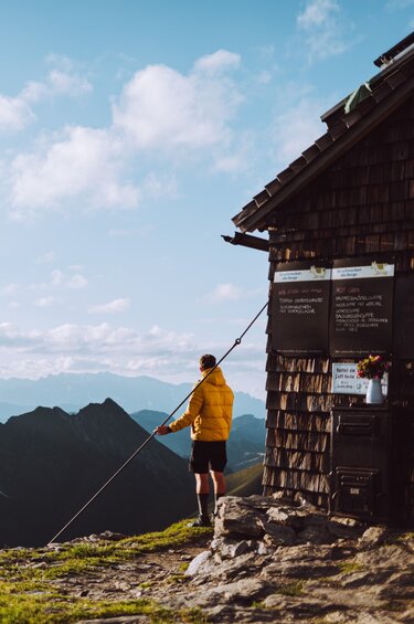 Wanderer vor einer Berghütte mit atemberaubendem Panorama der umliegenden Gipfel und Täler. | © SalzburgerLand Tourismus - Denis Cebulec