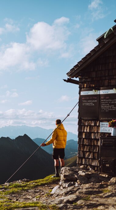Wanderer vor einer Berghütte mit atemberaubendem Panorama der umliegenden Gipfel und Täler. | © SalzburgerLand Tourismus - Denis Cebulec