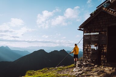 Wanderer vor einer Berghütte mit atemberaubendem Panorama der umliegenden Gipfel und Täler. | © SalzburgerLand Tourismus - Denis Cebulec