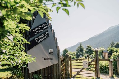 Eingangsschild des Hollersbacher Kräutergartens mit Bergpanorama im Hintergrund. | © Chris Perkles