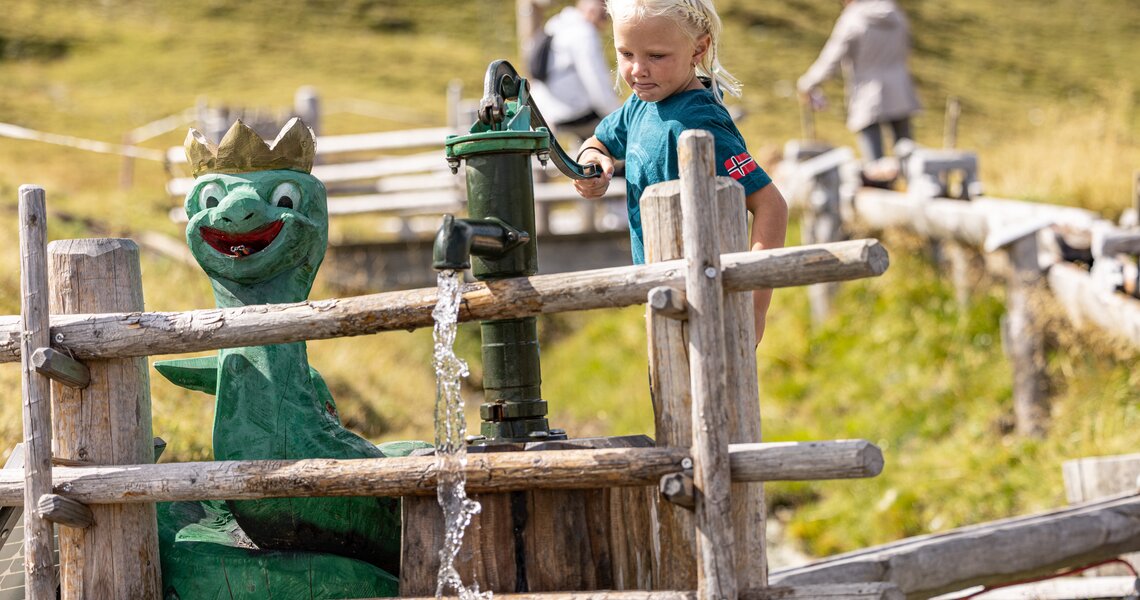 Kind bedient Wasserpumpe neben Drachenfigur auf einem alpinen Spielplatz. | © Zillertal Arena
