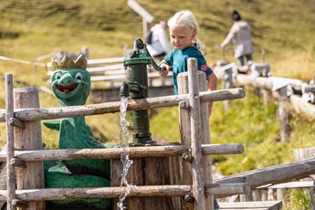 Kind bedient Wasserpumpe neben Drachenfigur auf einem alpinen Spielplatz. | © Zillertal Arena