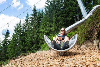 Mutter und Kind genießen gemeinsam eine Rutschfahrt auf einer großen Metallrutsche. | © Wildkogel-Arena Neukirchen & Bramberg
