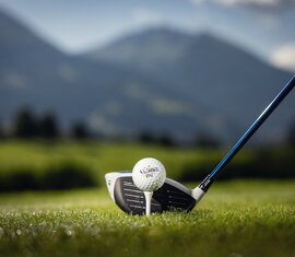 Ein Golfball auf einem Tee, dahinter grüne Wiesen und Berge. | © SalzburgerLand Tourismus