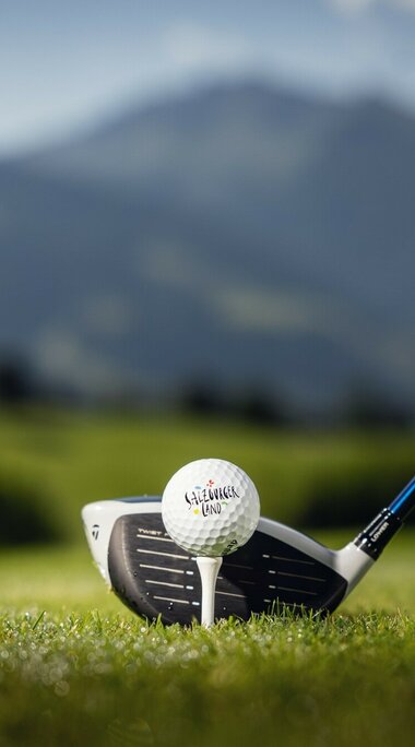 Ein Golfball auf einem Tee, dahinter grüne Wiesen und Berge. | © SalzburgerLand Tourismus