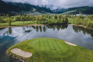 Eine Golfinsel inmitten eines Sees, mit malerischen Bergen im Hintergrund. | © Expa Pictures Original