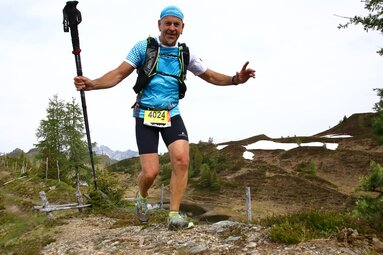 Trail runner with hiking poles smiling while running along an alpine trail. | © TVB Großarltal