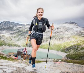 Lächelnder Läufer bei einem Berglauf vor alpiner Kulisse und einem See im Hintergrund. | © Philipp Reiter