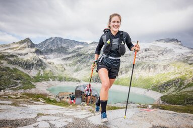 Lächelnder Läufer bei einem Berglauf vor alpiner Kulisse und einem See im Hintergrund. | © Philipp Reiter