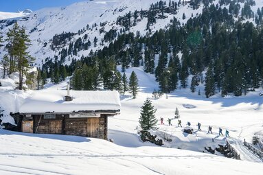 Winter hikers crossing a bridge in a snow-covered mountain landscape. | © Ole Zimmer