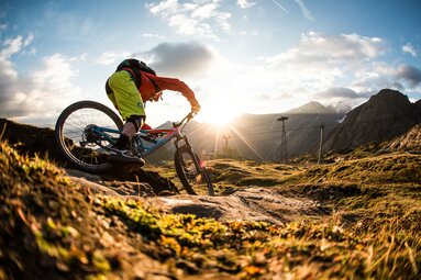 Mountainbiker bei Sonnenuntergang auf alpinem Trail mit Bergen im Hintergrund. | © SalzburgerLand Tourismus