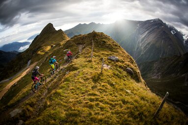 Drei Mountainbiker fahren einen schmalen Grat entlang, umgeben von alpiner Landschaft. | © SalzburgerLand Tourismus