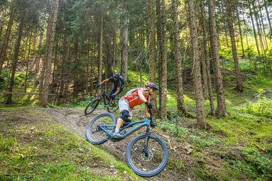 Zwei Mountainbiker auf einem Waldpfad, Sonnenstrahlen durch die Bäume brechen die Szene auf. | © SalzburgerLand Tourismus