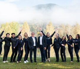 Gruppe fröhlicher Menschen in Businesskleidung posiert vor einer herbstlichen Berglandschaft. | © Foto Christine