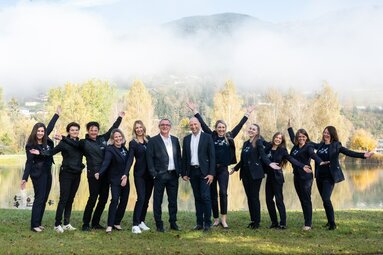 Gruppe fröhlicher Menschen in Businesskleidung posiert vor einer herbstlichen Berglandschaft. | © Foto Christine
