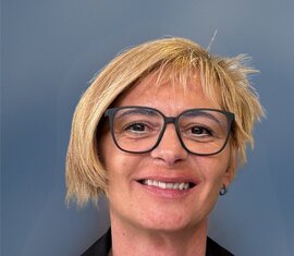 Porträt einer lächelnden Frau mit kurzen blonden Haaren in dunkler Kleidung vor blauem Hintergrund. | © Ferienregion Nationalpark Hohe Tauern