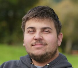 Junger Mann mit dunkler Kapuzenjacke lächelt dezent im Freien. | © Nationalparkverwaltung Salzburg