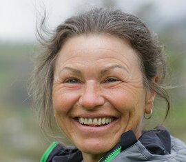 Frau mit grauen Haaren und Outdoor-Jacke lacht herzlich vor unscharfem Naturhintergrund. | © Nationalparkverwaltung Salzburg