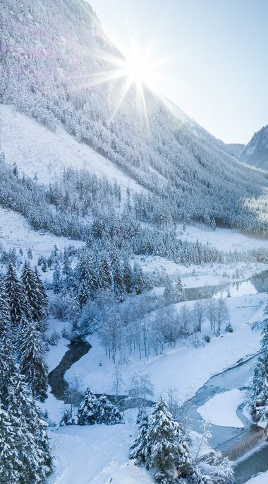 Sonnenaufgang über verschneitem Tal mit Fluss und Tannenwald. | © Ferienregion Nationalpark Hohe Tauern - Daniel Breuer