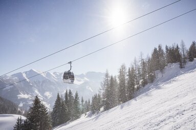 Gondelbahn fährt bei Sonnenschein über verschneiten Hang. | © Ferienregion Nationalpark Hohe Tauern - Branislav Rohal