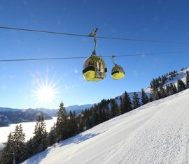 Gelbe Gondeln schweben über einer verschneiten Piste bei Sonnenschein. | © Tourismusverband Großarltal