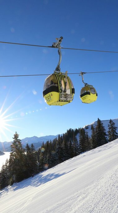 Gelbe Gondeln schweben über einer verschneiten Piste bei Sonnenschein. | © Tourismusverband Großarltal