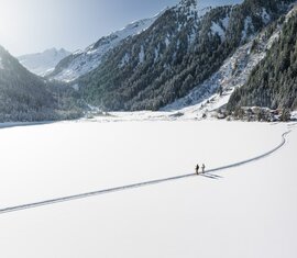 Zwei Menschen wandern über einen verschneiten, zugefrorenen See. | © Ferienregion Nationalpark Hohe Tauern - Daniel Breuer
