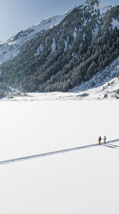 Zwei Menschen wandern über einen verschneiten, zugefrorenen See. | © Ferienregion Nationalpark Hohe Tauern - Daniel Breuer