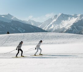 Zwei Langläufer bei Sonnenschein vor verschneiten Bergen. | © Ferienregion Nationalpark Hohe Tauern - Mathäus Gartner