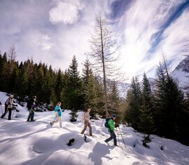 Gruppe beim Schneeschuhwandern vor verschneiten Bergen im Sonnenschein. | © NPHT- Florian Kreidl-Glueck