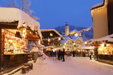 Verschneiter Weihnachtsmarkt mit Lichtern und Besuchern vor festlich geschmückten Hütten. | © Tourismusverband Großarltal