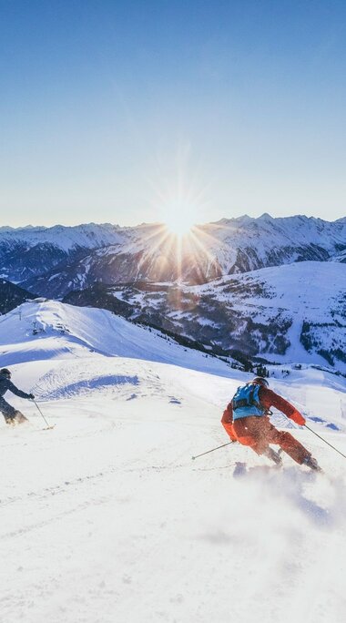 Zwei Skifahrer fahren bei Sonnenuntergang durch tiefen Schnee in den Alpen. | © Zillertal Arena