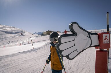Kind auf Skipiste gibt einem riesigen Daumen aus Kunststoff ein High Five. | © Wildkogel-Arena Neukirchen & Bramberg