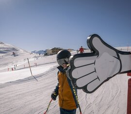 Kind auf Skipiste gibt einem riesigen Daumen aus Kunststoff ein High Five. | © Wildkogel-Arena Neukirchen & Bramberg