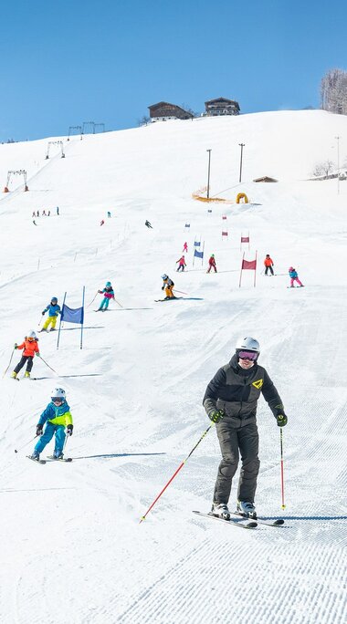 Skischüler fahren Slalom auf einer sonnigen, präparierten Piste. | © TVB Piesendorf Niedernsill - Harry Liebmann