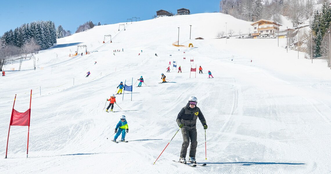 Ski students practicing slalom on a sunny, groomed slope. | © TVB Piesendorf Niedernsill - Harry Liebmann