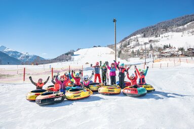 Kinder beim Snowtubing im Schnee vor winterlicher Bergkulisse. | © TVB Piesendorf Niedernsill - Harry Liebmann