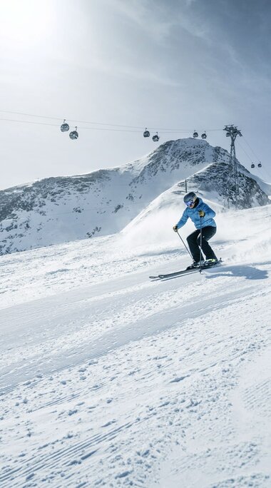 Zwei Skifahrer auf Abfahrt mit Gondeln und Berggipfeln im Hintergrund.  | © Kitzsteinhorn