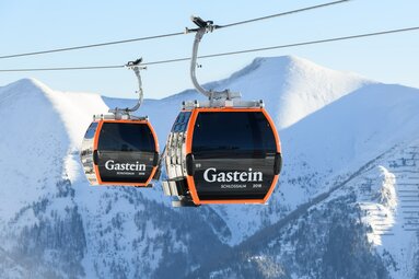 Zwei Gondeln der Schlossalmbahn in Gastein vor verschneiten Bergen.