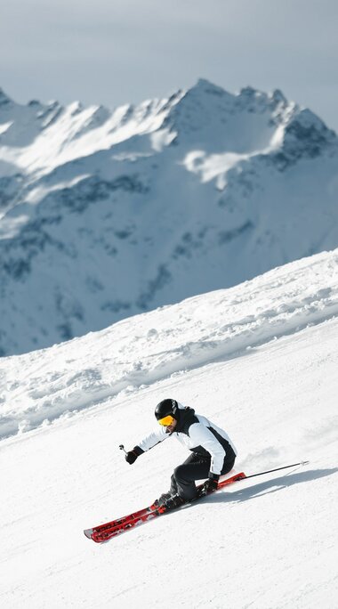 Skifahrer fährt schwungvoll eine Piste vor beeindruckender Alpenkulisse hinunter. | © Ferienregion Nationalpark Hohe Tauern - Mathäus Gartner