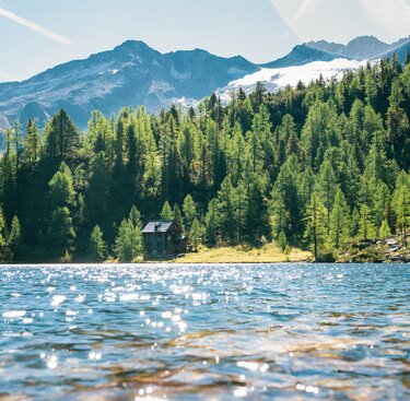 Ruhiger Bergsee mit einer Hütte am Ufer, umgeben von dichten Wäldern und Bergen. | © Salzburger Land Tourismus