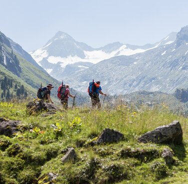 Wanderer mit Rucksäcken genießen den Ausblick auf ein weites Tal und schneebedeckte Berge. | © Nationalpark Hohe Tauern - Szopory