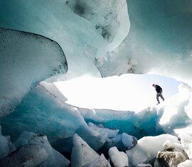 Wanderer im Inneren einer blauen Eishöhle, umgeben von bizarren Eisformationen. | © Nationalpark Hohe Tauern - Tobias Kaser