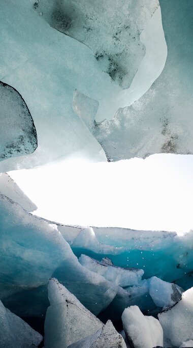 Wanderer im Inneren einer blauen Eishöhle, umgeben von bizarren Eisformationen. | © Nationalpark Hohe Tauern - Tobias Kaser