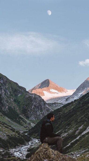 Alpental bei Sonnenaufgang mit Mond am Himmel und einem Wanderer im Vordergrund. | © Nationalpark Hohe Tauern - Tobias Kaser